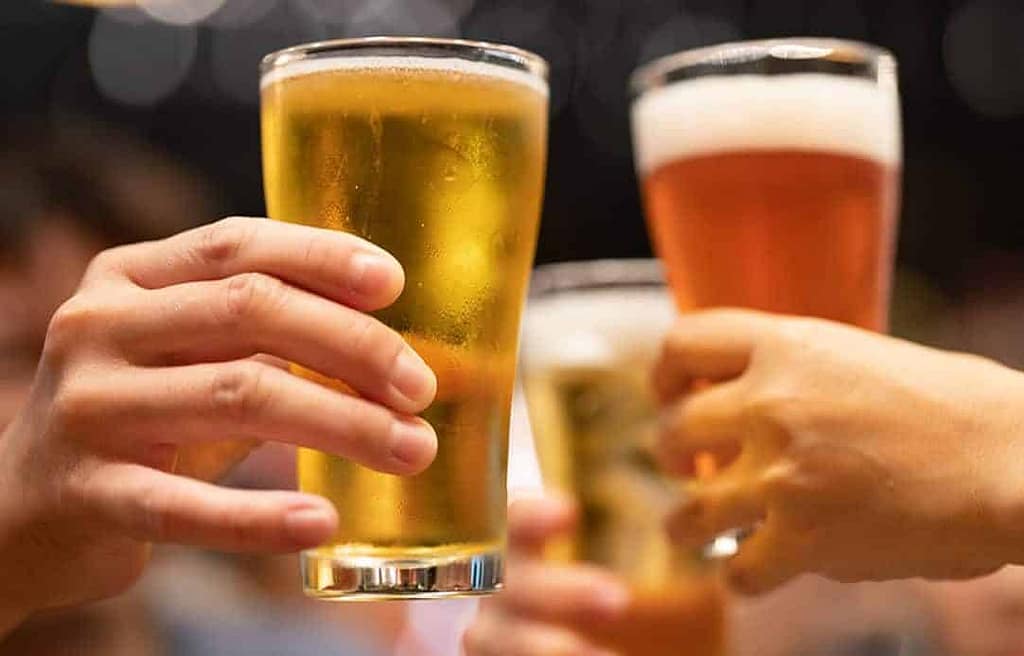 Three hands holding glasses of beer, toasting. One glass contains light beer and the other two contain amber beer with a foamy head—an ideal scene at Caliente Pizza & Drafthouse, the ultimate craft beer bar in Pittsburgh.