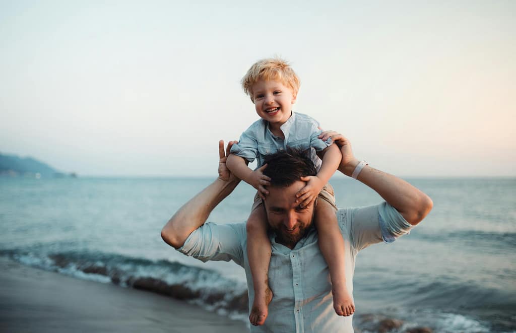 Happy son on father's shoulders at the beach