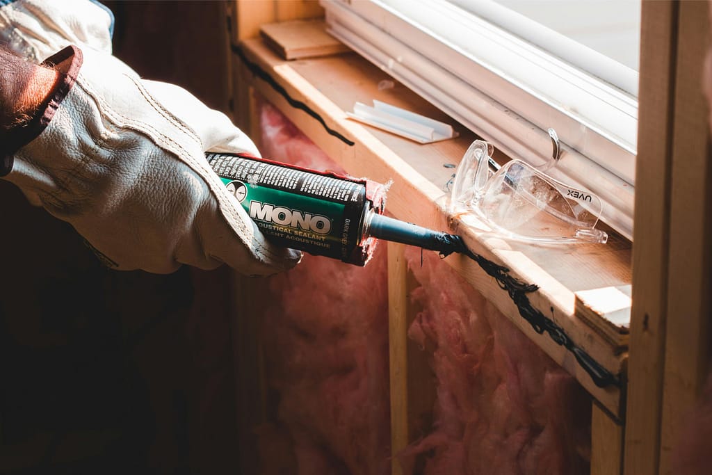 Person holding glue gun applying sealant under window