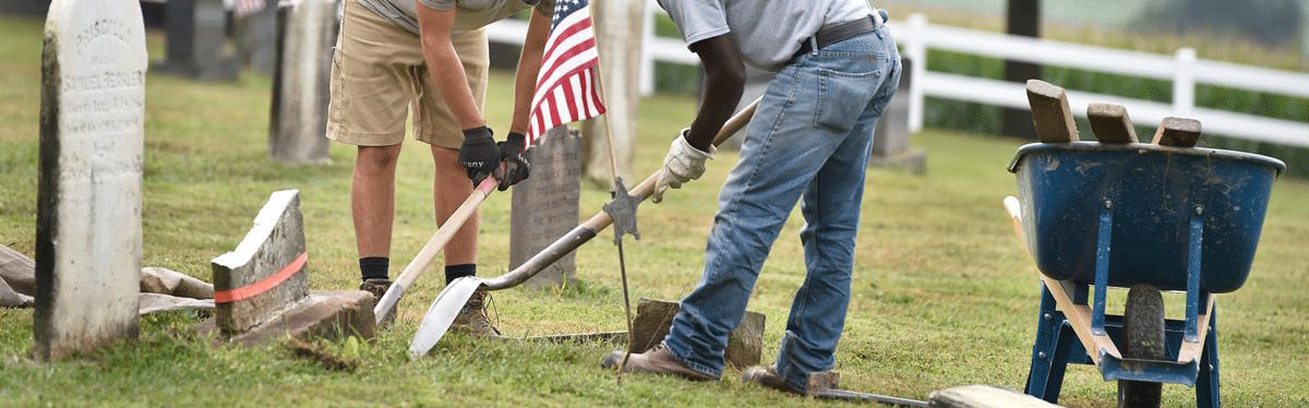 two men digging around headstone as part of repair process