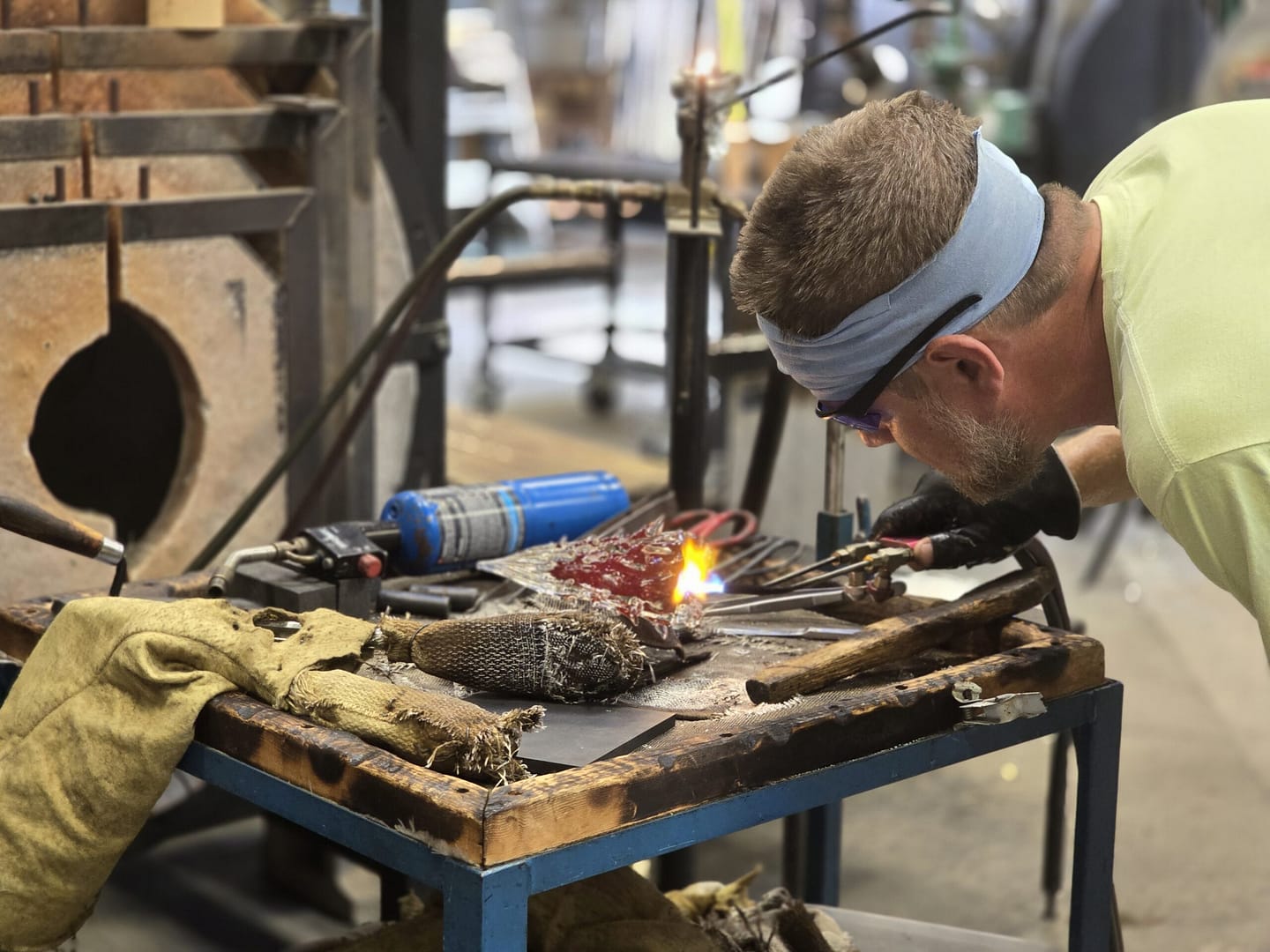 man looks closely at hot glass in glassblowing workshop