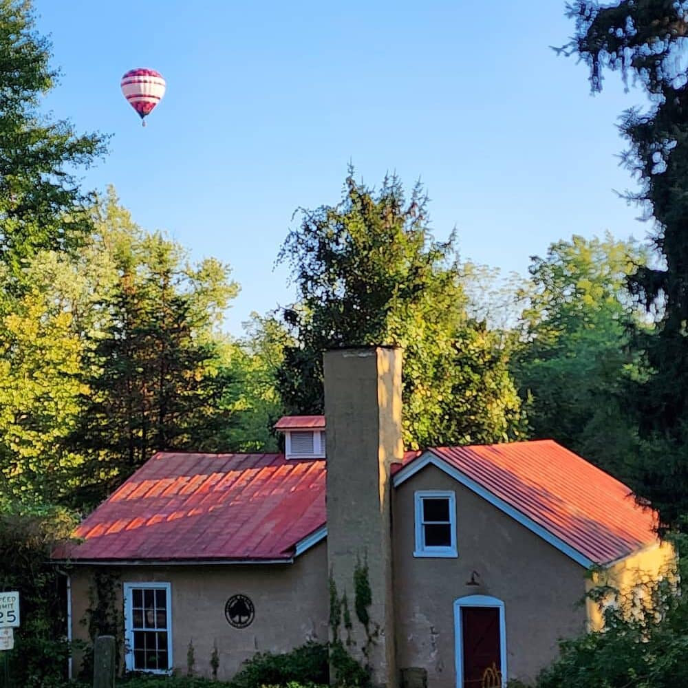 A hot air balloon flies over a preserved building in the historic village