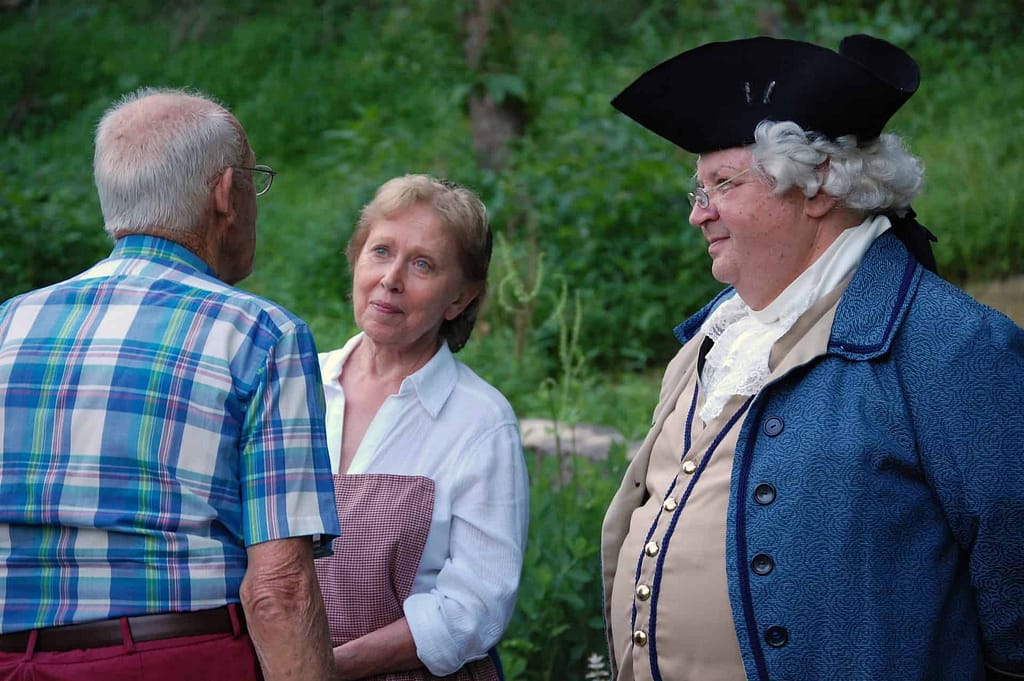 A volunteer presents information for a private group visit of community members in front of the preserved building in the village on the national register of historic places