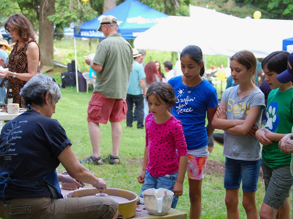 Youth participants watch a pottery wheel making demonstration at a community celebration event in the village on the national register of historic places