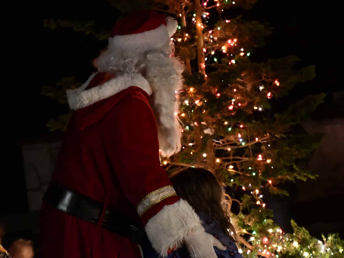 Santa and a young visitor enjoy a moment together in front of a lit holiday tree celebrating community in the village on the National Register of Historic Places
